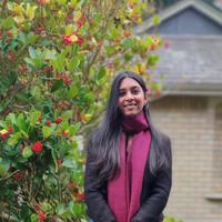 Woman with pick scarf standing next to green shrub